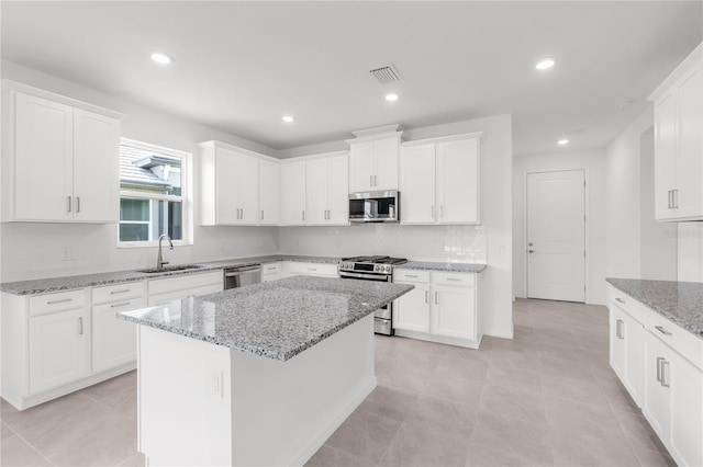 kitchen with light stone counters, a sink, decorative backsplash, stainless steel appliances, and white cabinetry