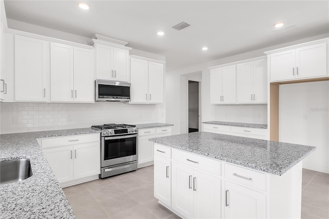 kitchen featuring tasteful backsplash, stainless steel appliances, white cabinetry, light stone countertops, and a kitchen island