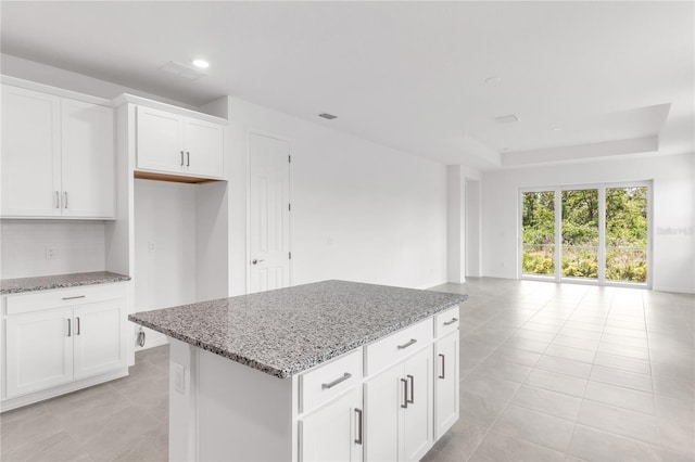 kitchen featuring light stone counters, backsplash, light tile patterned floors, a kitchen island, and open floor plan