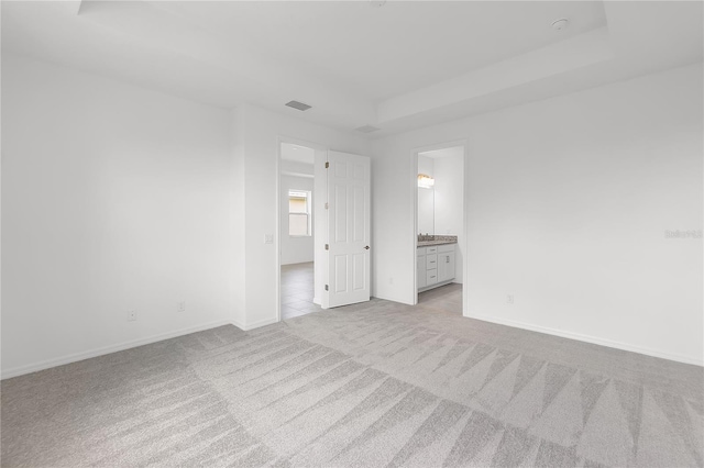 unfurnished bedroom featuring baseboards, ensuite bathroom, visible vents, and light colored carpet