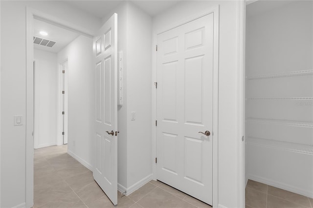 hallway with visible vents, baseboards, and light tile patterned floors