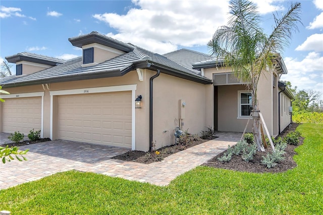 view of front of property featuring a tile roof, driveway, an attached garage, a front yard, and stucco siding
