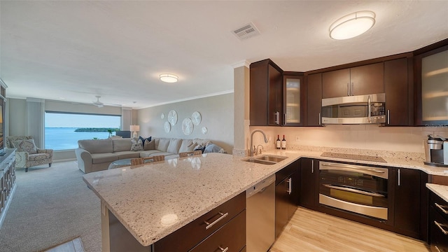kitchen featuring appliances with stainless steel finishes, a sink, dark brown cabinets, ornamental molding, and a peninsula
