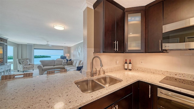 kitchen featuring a sink, dark brown cabinets, light stone counters, glass insert cabinets, and tasteful backsplash