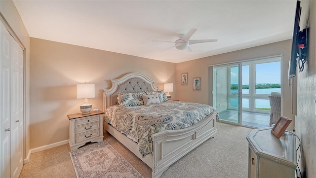 bedroom with access to exterior, light carpet, a water view, a ceiling fan, and baseboards