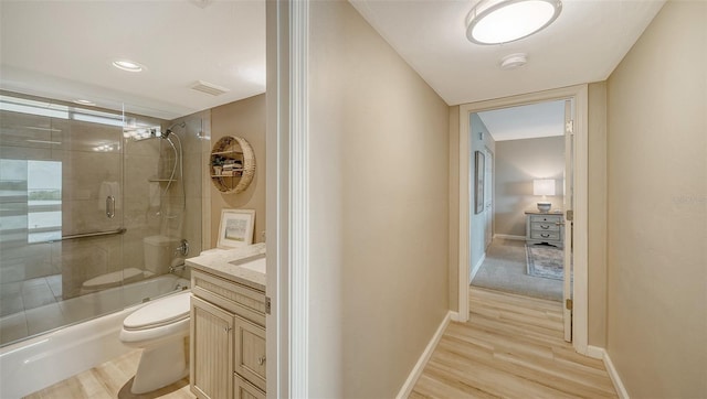 full bath featuring wood finished floors, toilet, shower / bath combination with glass door, vanity, and baseboards