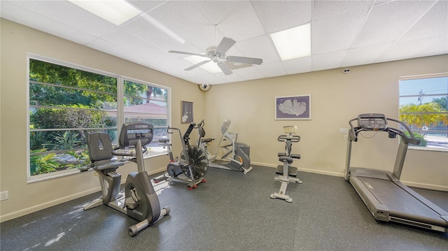 workout room featuring a drop ceiling, a ceiling fan, healthy amount of natural light, and baseboards