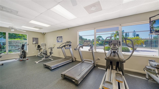 exercise room featuring ceiling fan, plenty of natural light, a paneled ceiling, and baseboards