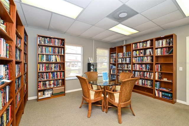 sitting room with bookshelves, carpet, a paneled ceiling, and baseboards