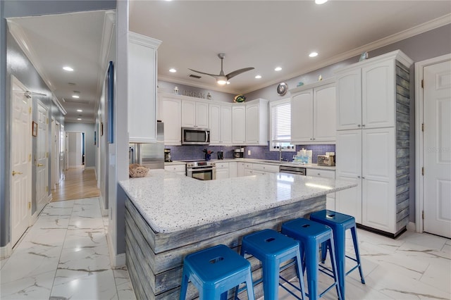 kitchen with a breakfast bar, marble finish floor, appliances with stainless steel finishes, and crown molding