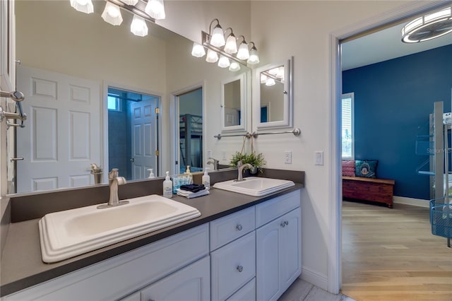 ensuite bathroom with wood finished floors, baseboards, a sink, and double vanity