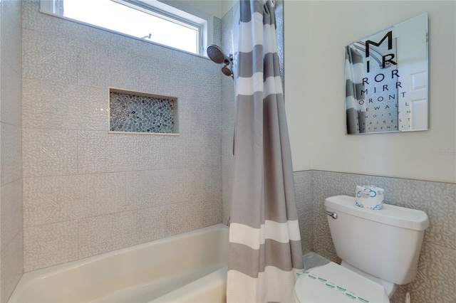 bathroom with tile walls, shower / bath combo with shower curtain, a wainscoted wall, and toilet
