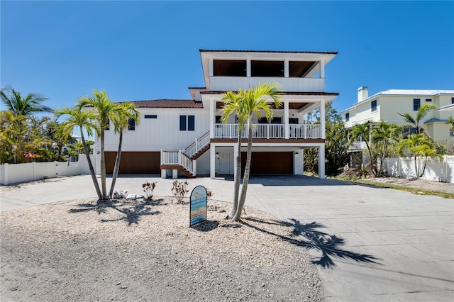 coastal inspired home with stairs, fence, concrete driveway, an attached garage, and covered porch
