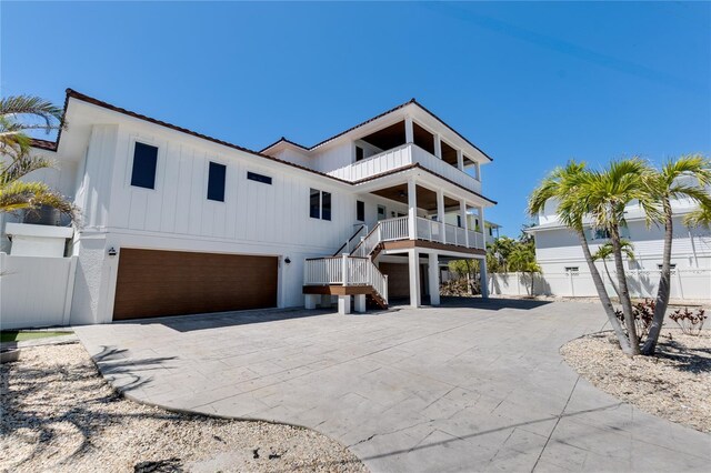 view of front of home with a balcony, driveway, board and batten siding, an attached garage, and fence