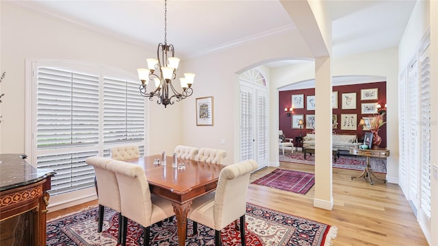 dining space with crown molding, light wood finished floors, arched walkways, a chandelier, and baseboards