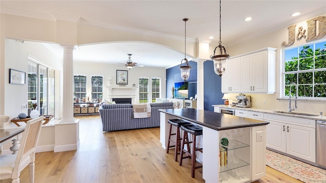 kitchen featuring crown molding, a sink, a ceiling fan, decorative columns, and light wood-type flooring
