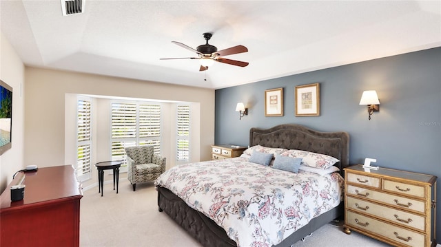 bedroom featuring ceiling fan, a tray ceiling, light colored carpet, and visible vents