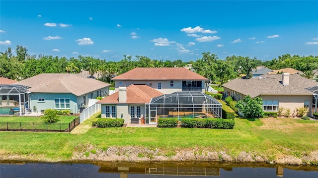 rear view of house with a fenced backyard, glass enclosure, a water view, and a lawn