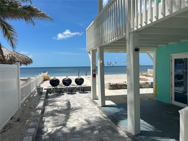 view of patio / terrace featuring a beach view, a balcony, a water view, and fence