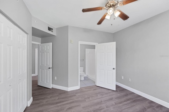 unfurnished bedroom with a closet, wood finished floors, baseboards, and ensuite bath