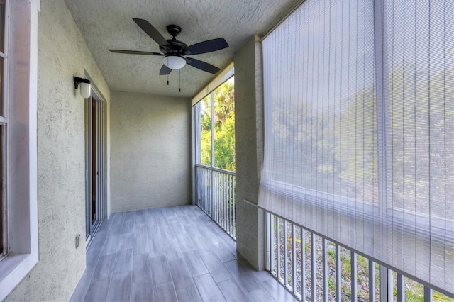 unfurnished sunroom with ceiling fan, wood finished floors, a textured ceiling, and a textured wall