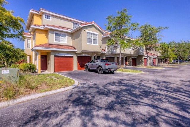 view of front of house with an attached garage, a tiled roof, asphalt driveway, and stucco siding