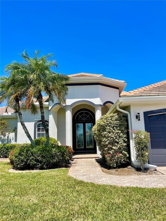2980 Seasons Blvd, Sarasota, FL 34240 - view of exterior entry with stucco siding, a tiled roof, a yard, french doors, and a garage