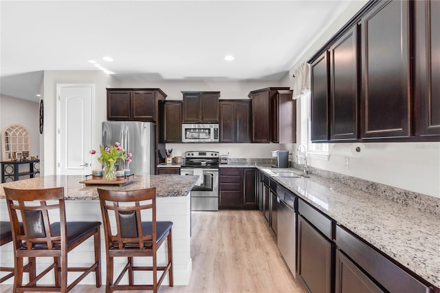 10806 52nd Ct E, Parrish, FL 34219 - kitchen with stainless steel appliances, light wood-style floors, a breakfast bar, dark brown cabinetry, and light stone counters