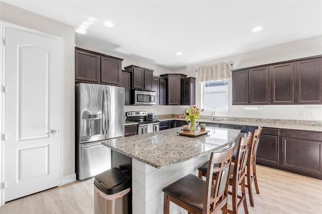 10806 52nd Ct E, Parrish, FL 34219 - kitchen with appliances with stainless steel finishes, dark brown cabinetry, light stone counters, a center island, and light wood-type flooring