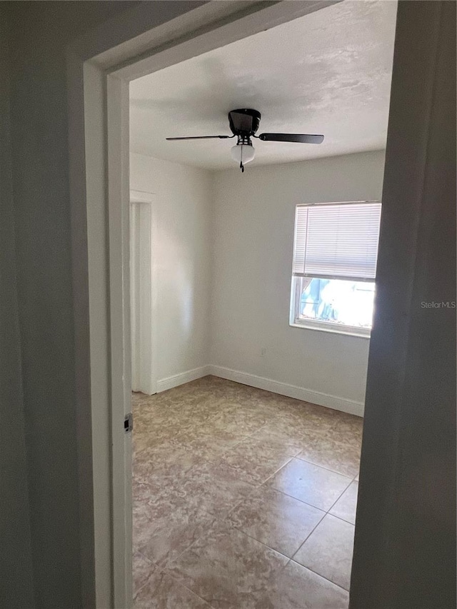 empty room featuring baseboards, a ceiling fan, and tile patterned flooring