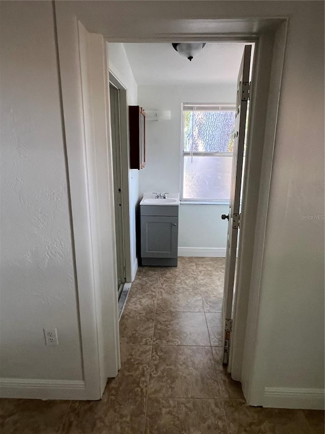 hall featuring baseboards and a sink