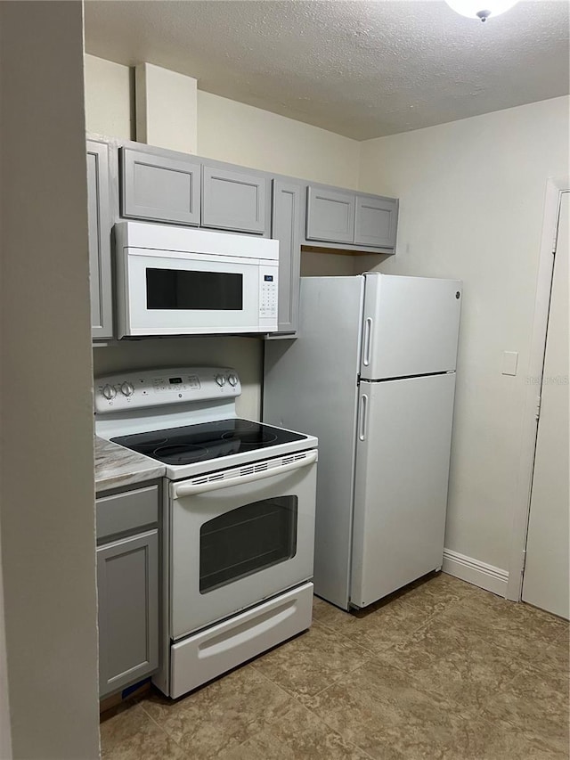 kitchen featuring gray cabinets, a textured ceiling, white appliances, and light countertops