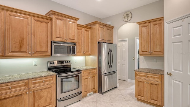 5355 Anthony Ln, Sarasota, FL 34233 - kitchen featuring stainless steel appliances, arched walkways, light stone countertops, and light tile patterned floors