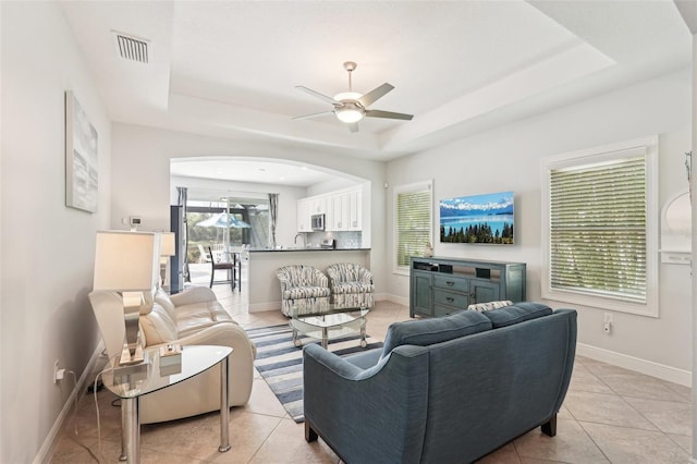 living area featuring baseboards, visible vents, a raised ceiling, a ceiling fan, and light tile patterned flooring