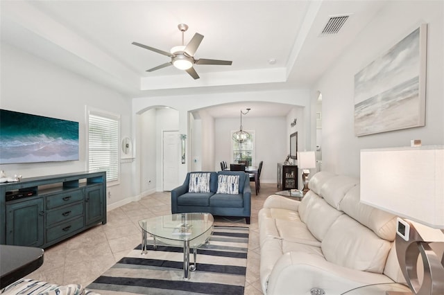living room featuring light tile patterned floors, a raised ceiling, a ceiling fan, visible vents, and arched walkways
