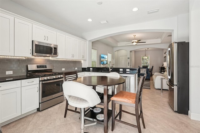 kitchen featuring stainless steel appliances, a ceiling fan, backsplash, white cabinetry, and arched walkways