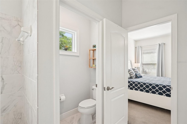 ensuite bathroom with tiled shower, marble finish floor, toilet, ensuite bathroom, and baseboards