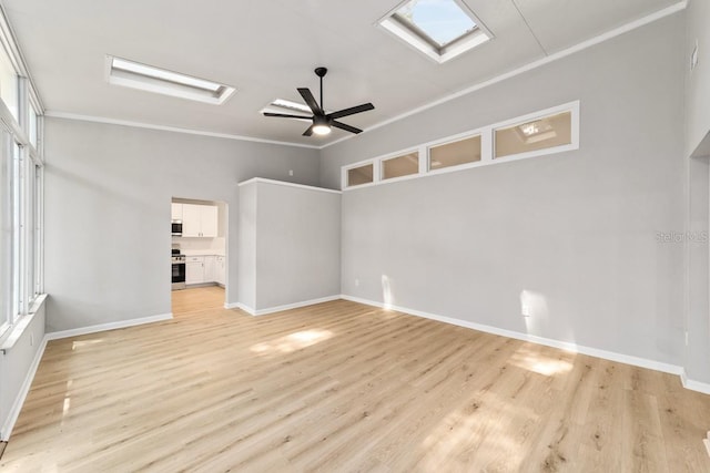 empty room featuring light wood-type flooring, baseboards, a skylight, a ceiling fan, and crown molding