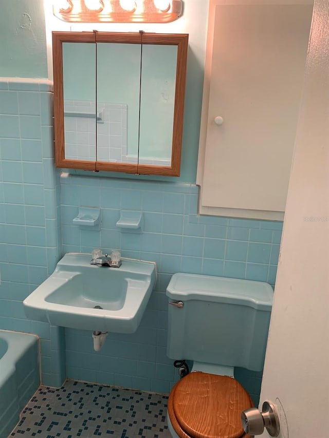 bathroom featuring a sink, a bathtub, toilet, tile walls, and tile patterned flooring