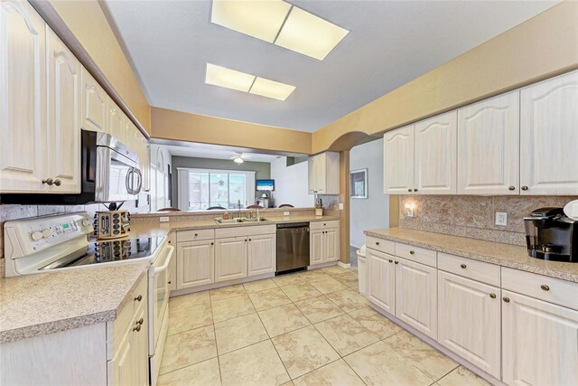 kitchen with tasteful backsplash, a sink, arched walkways, stainless steel appliances, and light countertops