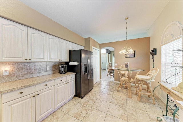 kitchen featuring tasteful backsplash, arched walkways, fridge with ice dispenser, an inviting chandelier, and white cabinetry