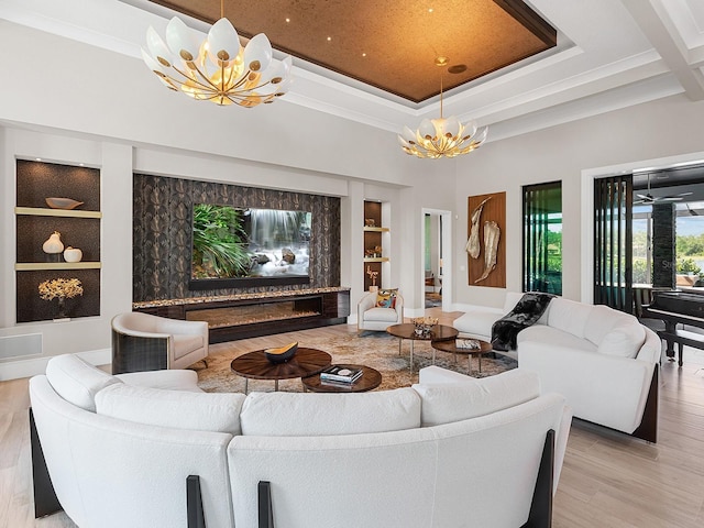 living room featuring light wood-style floors, ornamental molding, a towering ceiling, a notable chandelier, and built in shelves
