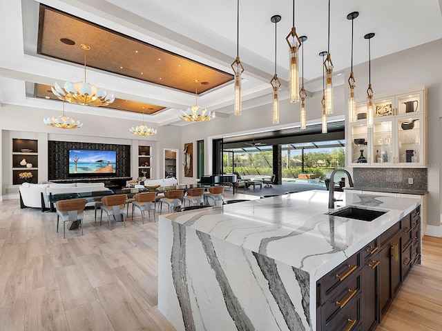 kitchen featuring a kitchen island with sink, a sink, light wood-style floors, a notable chandelier, and hanging light fixtures