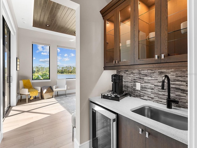 bar with beverage cooler, backsplash, a sink, baseboards, and light wood-type flooring