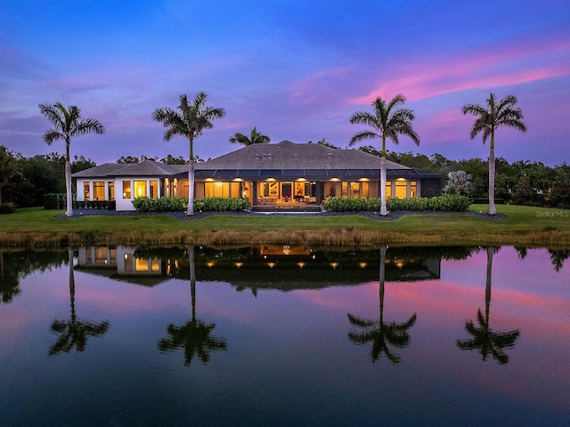 back of house at dusk with a yard and a water view