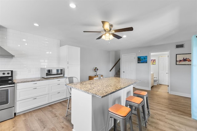 14519 Catalina Cir, Seminole, FL 33776 - kitchen with a ceiling fan, stainless steel electric range, a kitchen bar, white cabinets, and visible vents