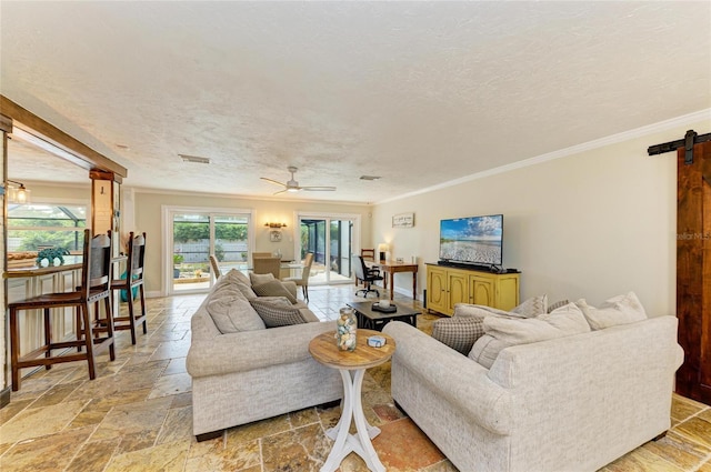 living room with a textured ceiling, a barn door, stone tile floors, ceiling fan, and ornamental molding