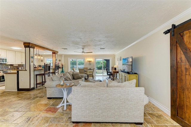 living room with a barn door, stone tile floors, a ceiling fan, and baseboards