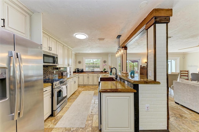 kitchen featuring crown molding, a textured ceiling, wooden counters, stone tile flooring, and appliances with stainless steel finishes