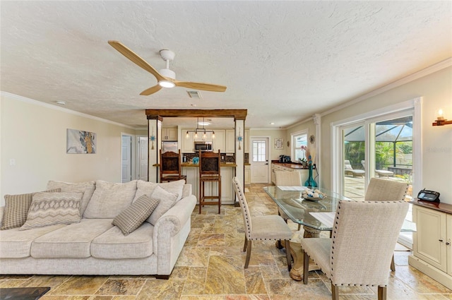 living room with ceiling fan, stone tile flooring, a textured ceiling, and ornamental molding